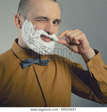 Hipster. Funny portrait of trendy man making moustache and beard of shaving foam and gives wink, toned.