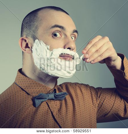 Hipster. Funny portrait of trendy man making moustache and beard of shaving foam, toned.