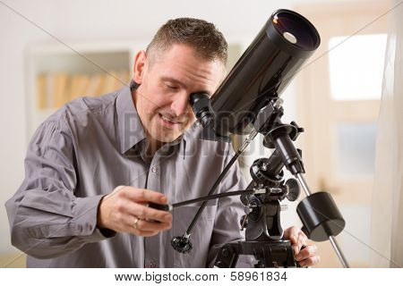 Man looking skyward through astronomical telescope standing near a window