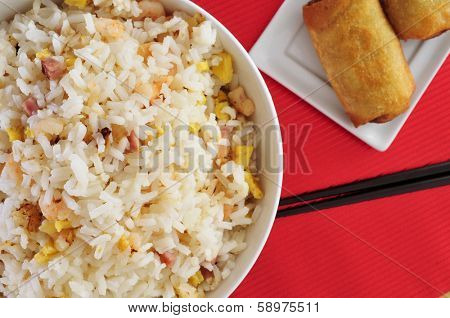 closeup of a bowl with appetizing chinese fried rice and some springrolls in a plate on a set table
