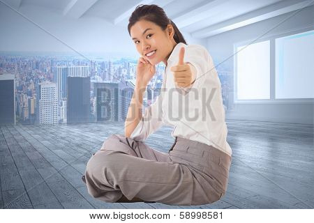 Businesswoman sitting cross legged showing thumb up against city scene in a room