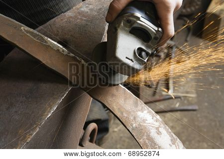 Blacksmith using angle grinder on edge of metal tool in workshop
