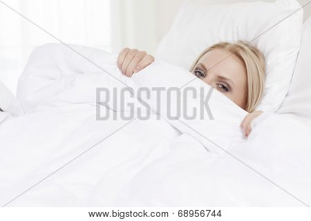 Portrait of young woman hiding under bedsheet