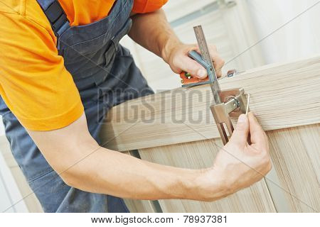 Close-up carpenter hands with doorlock during lock process installation into wood door