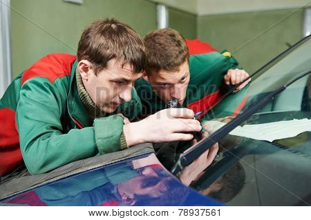 Automobile glazier repairman teaching or discussing with partner windscreen repair of a car in auto service station garage