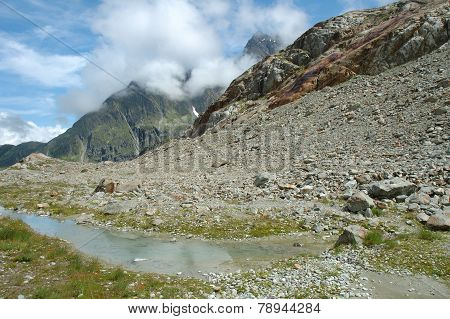 Stones And Water In Valley Nearby Glacier In Alps In Switzerland