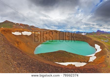 July in Iceland. Lake in the crater of an extinct volcano. Lake water bright green color. On the shores lie snowfields from last year