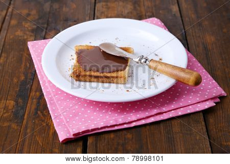 Toast bread spread with chocolate on plate with knife and napkin on wooden table background