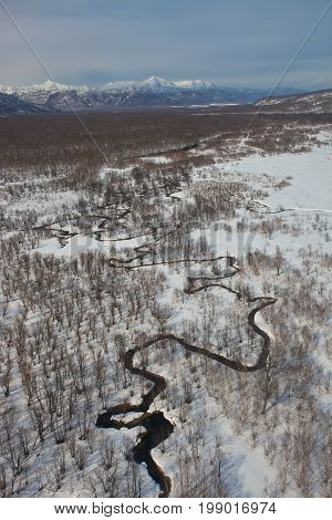 The floodplain of the river meanders in a mountain snowy tundra of Kamchatka Peninsula. The view from the helicopter on the meandering small river in Eastern Russia.