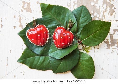 Beautiful and tasty dessert in the form of heart lies on green leaves on an old wooden background.