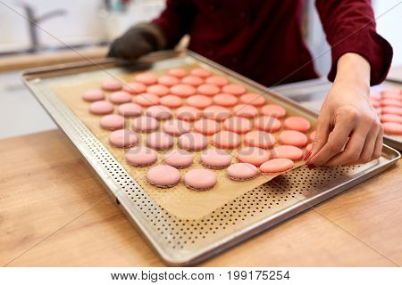 cooking, confectionery and people concept - chef with macarons on oven tray at bakery