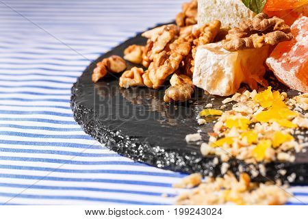 A beautiful composition of turkish delights, lokum or rahat lokum, walnuts and vivid green leaves of mint on a dark glass plate on a striped background, close-up. Sweets concept. Copy space.