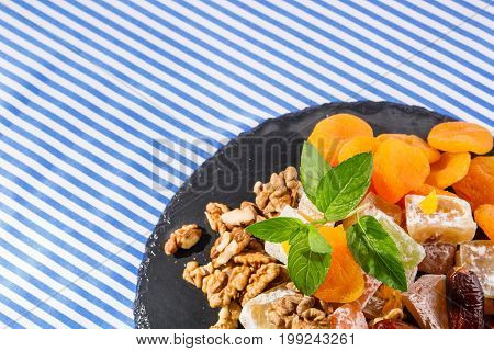 Closeup of dry apricots, turkish delight, lokum or rahat lokum, sweet date fruits, walnuts, bright aromatic leaves of mint on a striped background, top view. Sweets concept.