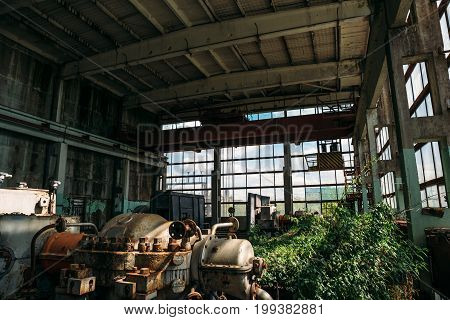 Big abandoned industrial factory or plant with steel equipment, overgrown with plants, post apocalipse concept