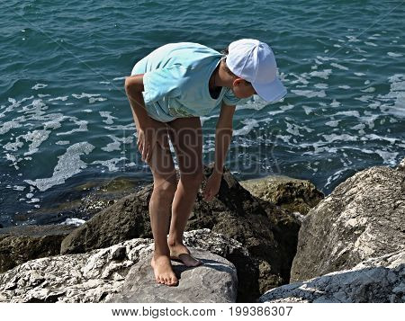 The azure sea of the Venetian Riviera foams off the coast. It's a warm June day. On large boulders, a tanned, long-legged young man in a blue T-shirt and white cap hunts for crabs.