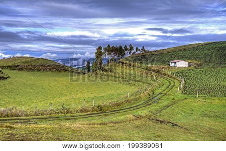 View of a house, a road and a green mountain range, part of the Ecuadorian Andes, with a beautiful sunny and cloudy sky. Cayambe, Ecuador.