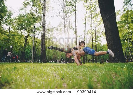 Teenagers couple in a beautiful park having fun. The boy is doing flexing exercise, and the girl is upon him.
