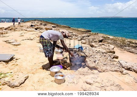 Tour to the sandy Bazaruto island in Bazaruto Archipelago with local people grilling barracuda fish next to the ocean. Mozambique, Africa.February 2017