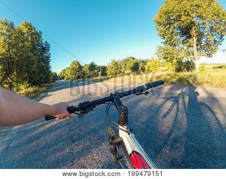 The girl stands near the bicycle and holds the steering wheel with one hand on an asphalt road in nature On a sunny summer evening. Action camera go pro. Copy space.