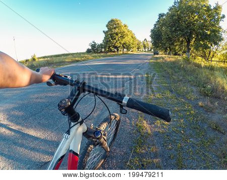 The girl stands near the bicycle and holds the steering wheel with one hand on an asphalt road in nature On a sunny summer evening. Action camera go pro. Copy space.