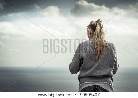 Pensive lonely woman looking with hope at horizon with bright sunlight in dramatic sky with effect of light at the end of tunnel