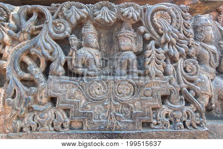 Two Hindu gods in carved royal cart. Lord Shiva and his wife Parvati on sculptured wall of 12th centur Hindu Hoysaleshwara temple in Halebidu, India.