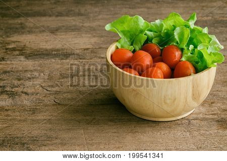 Fresh tomato and lettuce in wood bowl put on wood table. Side view of tomato and green oak lettuce with copy space for background. Fresh green oak lettuce and tomato prepare for cooking. Green lettuce and red tomato concept for background.
