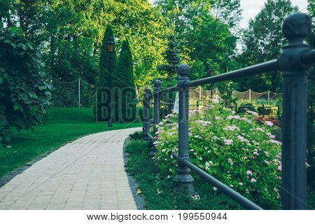 empty summer park with sidewalk and metal fence in the evening