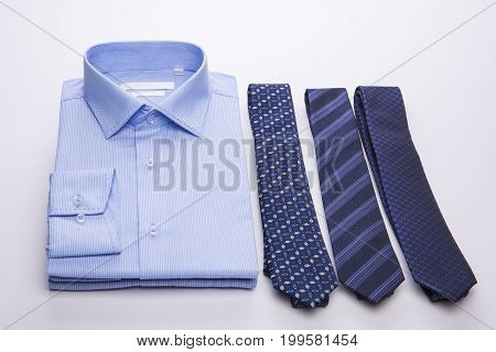 Three blue men's shirts folded in a pack and ties on a white background.