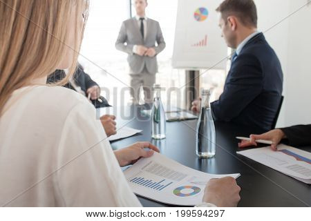 Group of business people at meeting watching presentation of reports in diagrams and graphs at flip chart in offfice