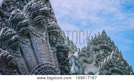 Skulptur of many snake heads. Shape of ancient stone temple in background.