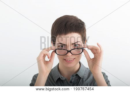 Young female teacher in a plaid shirt looking over her glasses on white background