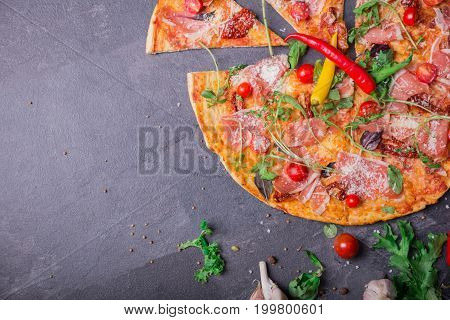 A top view of an Italian traditional pazza margherita with big slices of meat, halthy vegetables and double cheese on a dark stone background. Cooking concept. Copy space.