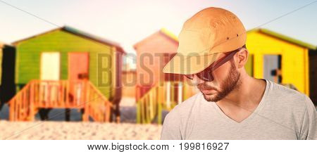 Model wearing cap and sunglasses against multi colored huts on sand against clear sky
