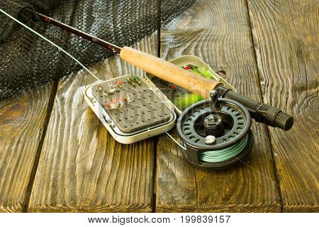 Fly fishing rod ,flie and a landing net on the old wooden table. All ready for fishing.