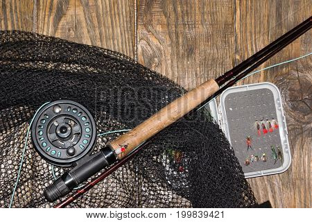 Fly fishing rod ,flie and a landing net on the old wooden table. All ready for fishing.