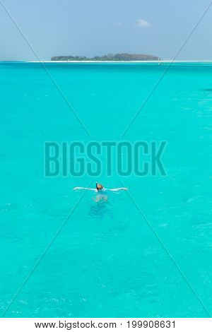 Woman snorkeling in clear shallow sea of tropical lagoon with turquoise blue water and coral reef, near exotic island. Mnemba island, Zanzibar, Tanzania.