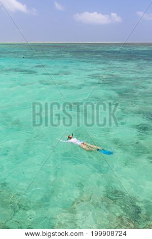 Woman snorkeling in clear shallow sea of tropical lagoon with turquoise blue water and coral reef, near exotic island. Mnemba island, Zanzibar, Tanzania.