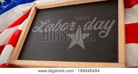 Digital composite image of happy labor day text with star shape against empty slate over american flag  on table