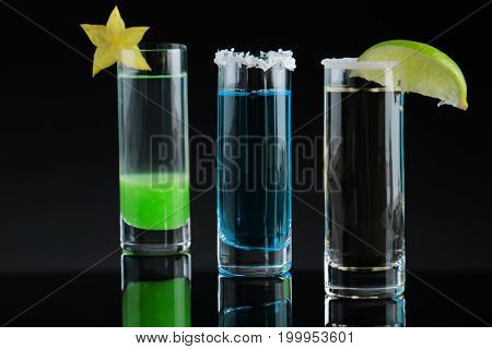 A close-up picture of three bright shots on a black background. Tequila drinks with decorative exotic fruits on a top of shot glasses. Strong alcoholic beverages for crazy parties. Copy space.