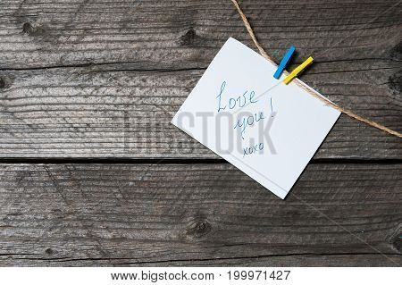 A White Sheet Of Paper Hanging On Clothespin, Place For Text, On A Background Of Old Wooden Planks.