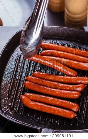 Young Woman In A Gray Apron Fries Sausages