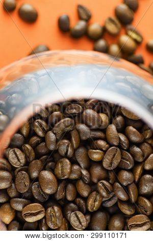 Close-up Top View Of Roasted Coffee Beans In A Glass Cup On An Orange Background. Vertical Photograp