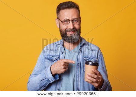 Delighted Positive Smiling Handsome Guy Holding Papercup Of Strong Coffee In One Hand, Pointing At I