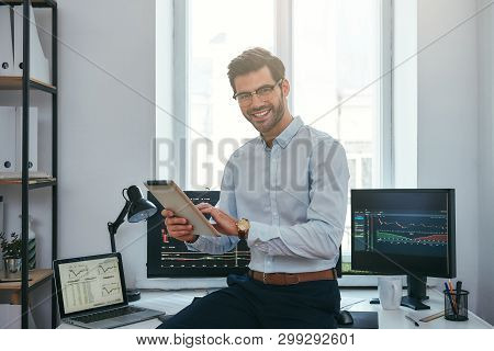 Business Success. Cheerful Young Trader In Formal Wear Is Holding Digital Tablet And Looking At Came