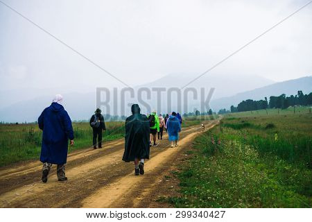 People Go Forward In Mountain Despite Bad Weather. Travelers Goes Upwards Along Road After Dog. Way 