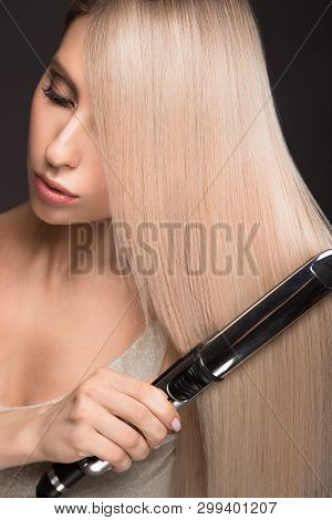 Beautiful Blond Girl With A Perfectly Smooth Hair, Classic Make-up With Curling Styler In The Hands.