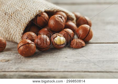 Macadamia Nuts Spilled Out Of The Bag On A Wooden Background Close-up With One Peeled Nut