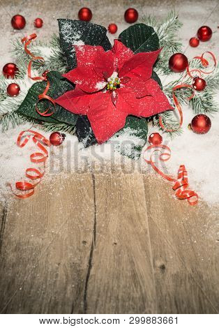 Christmas Background With Poinsettia, Red Baubles And Snow On Wood