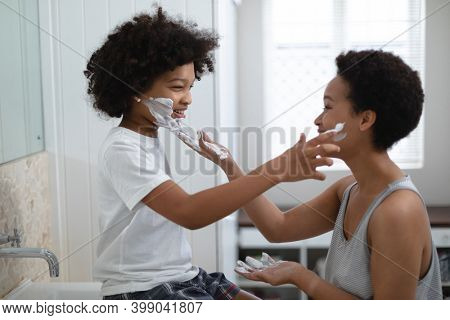 Mixed race woman playing with daughter in bathroom. putting cream on her face. self isolation quality time at home together during coronavirus covid 19 pandemic.